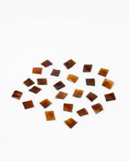 A small square semi-transparent brown adhesive tabs for tape-in hair extensions, scattered on a white background.