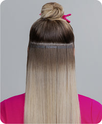 A back view of a woman’s head showcasing blonde hair with tape-in hair extensions.