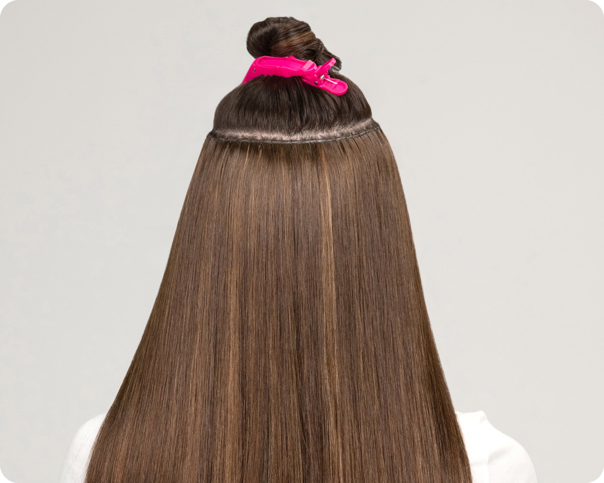 The back view of brown hair with weft extensions applied with her upper hair clipped up using a pink hair clip.