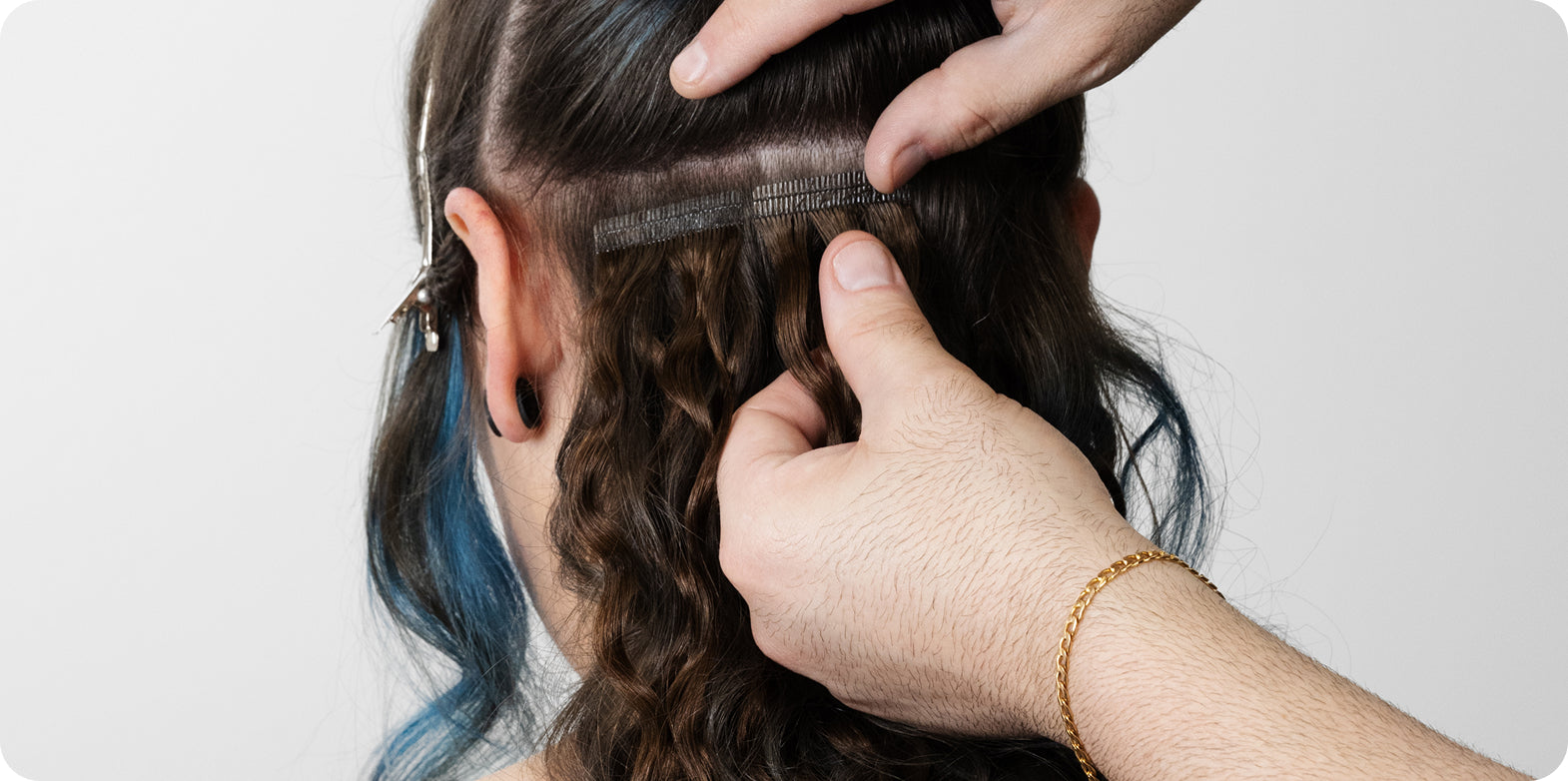 A hairdresser dresser applying wavy brown tape-in hair extensions for added length.